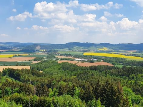 Vue panoramique de la campagne tchèque avec des champs, des forêts et des collines sous un ciel bleu avec des nuages blancs.