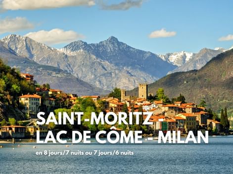 Village italien sur le lac de Côme avec toits en terre cuite et tour, dominé par des sommets alpins enneigés sous ciel bleu.