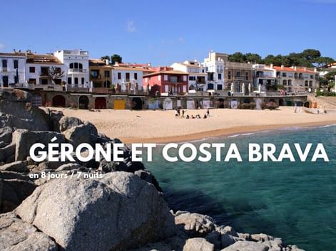 Plage de sable avec côte rocheuse et maisons méditerranéennes colorées sur la Costa Brava, Espagne. Eau turquoise claire et ciel bleu.