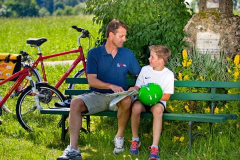Un père et son fils font une pause sur un banc et en profitent pour étudier l'itinéraire lors d'un séjour à vélo