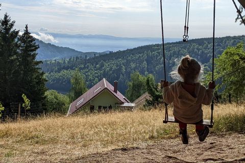 Petite fille se balançant sur une balançoire suspendue à un sapin devant un paysage de montagne vosgienne