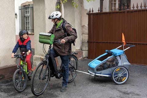 Un père et son fils à vélo, avec une petite fille en remorque, dans les rues de Strasbourg 