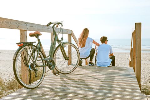 Couple de jeunes gens en pause sur une plage portugaise, devant un vélo électrique garé