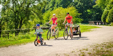 Jeune couple se promenant à vélo sur un chemin en Alsace, avec ses enfants en vélo à roulettes et dans une remorque