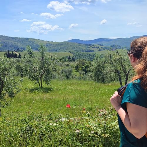 Randonneuse avec sac à dos orange contemplant les collines vertes de Toscane avec oliviers, montagnes lointaines et ciel bleu nuageux.