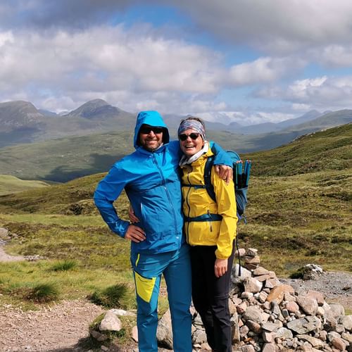 Deux randonneurs en vêtements de pluie colorés posent au sommet du Devils Staircase avec les montagnes écossaises en arrière-plan.