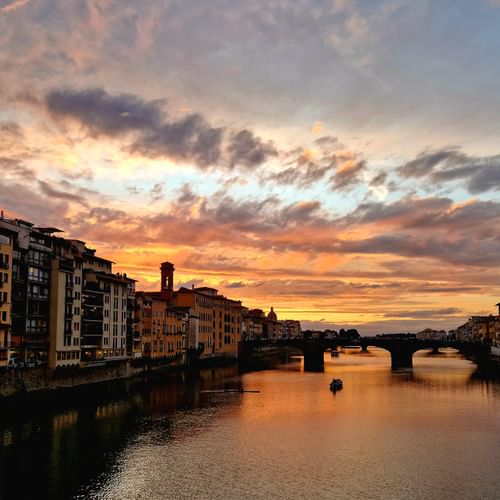 Coucher de soleil spectaculaire sur l'Arno à Florence avec des nuages colorés, des bâtiments historiques bordant les rives et un pont.