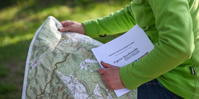 Randonneuse lisant une carte IGN et tenant un topoguide du circuit Vosges du Nord d'Espace Randonnée