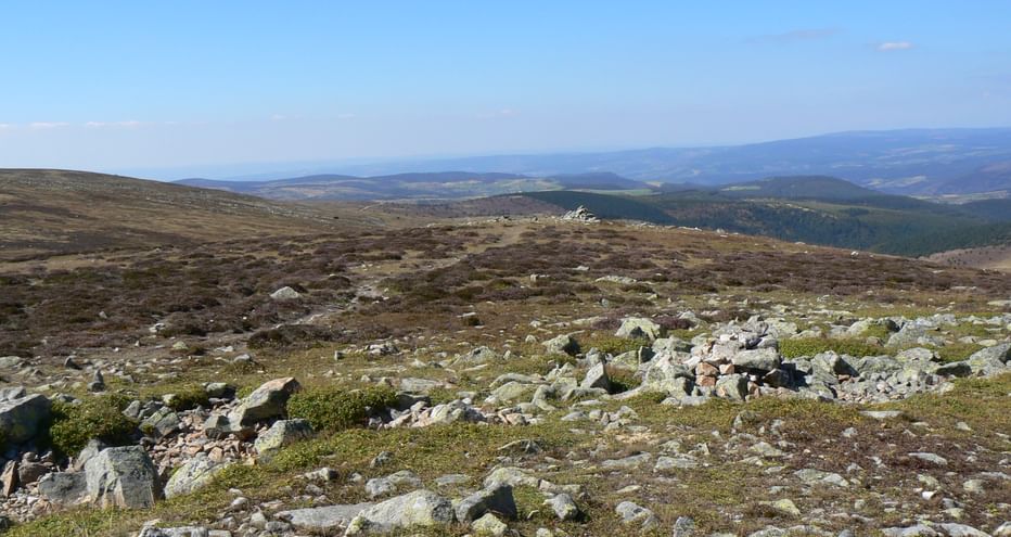 Paysage rocheux du sommet du Pic de Finiels sur le Mont Lozère avec pierres éparses, végétation basse et collines sous ciel bleu.
