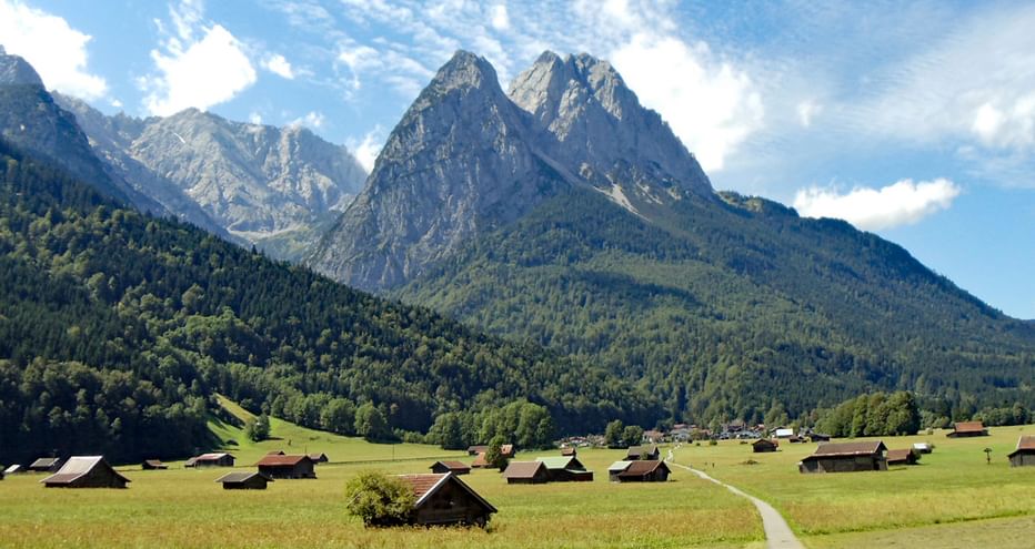 Vue panoramique sur la Zugspitze avec des pics rocheux spectaculaires dominant une vallée alpine verte parsemée de chalets en bois.