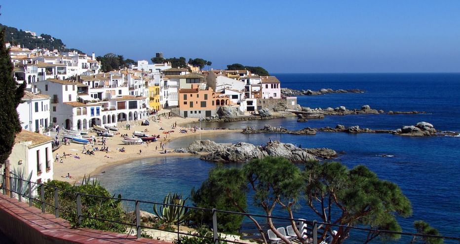 Vue panoramique du village balnéaire de Calella sur la Costa Brava avec bâtiments blancs, plage de sable, côte rocheuse et mer Méditerranée.