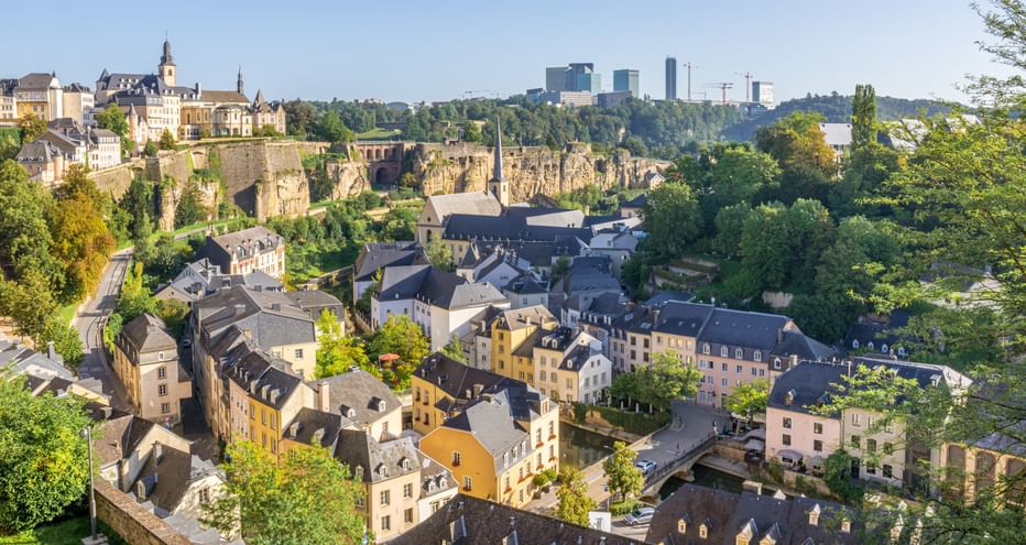 Vue panoramique de Luxembourg-Ville montrant des bâtiments historiques colorés dans la vallée, des murs de fortification anciens et une skyline moderne.