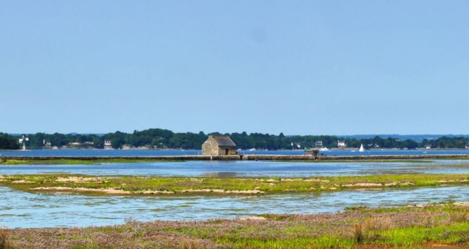 Vasières et marais salants sur l'île d'Arz avec structures en bois sur pilotis dans l'eau, côte lointaine et ciel bleu clair.
