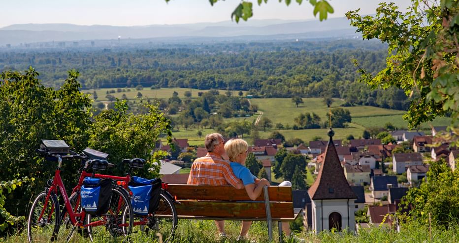 Couple de cyclotouristes profitent d'une pause détente sur un banc surplombant un vignoble de la Forêt-Noire du Sud