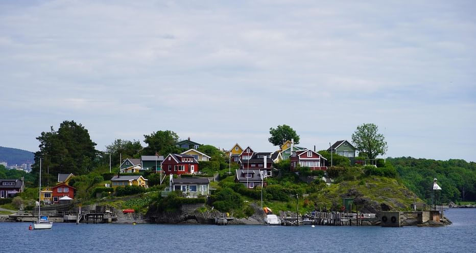 Petite île norvégienne avec maisons en bois colorées sur une colline surplombant un fjord. Bateaux amarrés aux quais, entourés de végétation.