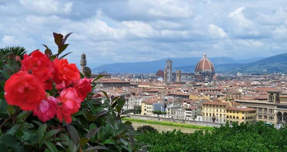 Fleurs rouges au premier plan avec le panorama de Florence derrière, montrant le dôme en terre cuite du Duomo et les clochers sous un ciel nuageux.