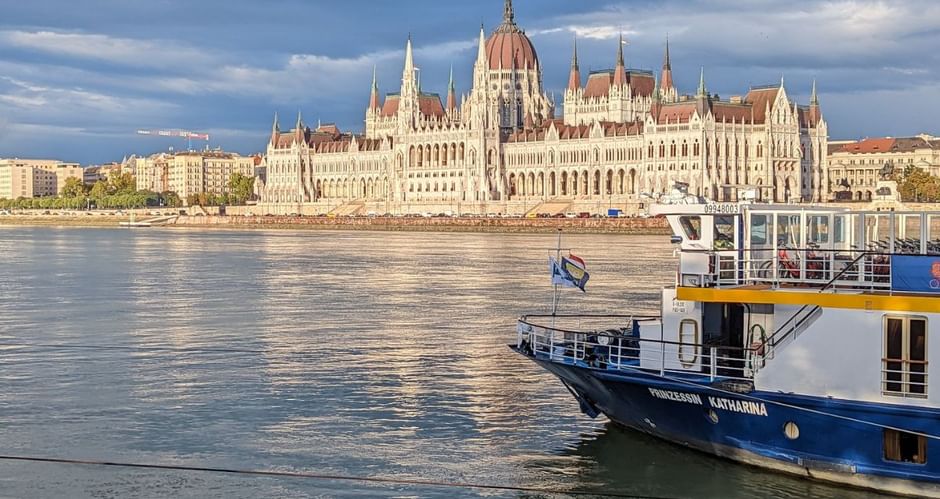 Bateau de croisière MS Princess Katharina sur le Danube avec le Parlement hongrois en arrière-plan sous un ciel nuageux.