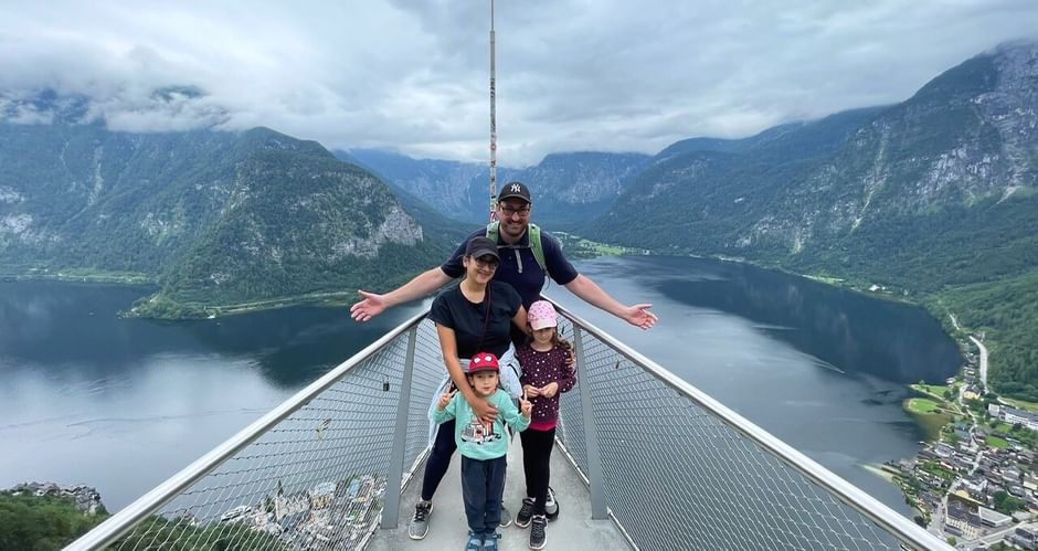 Famille de quatre personnes sur plateforme d'observation métallique surplombant le lac de Hallstatt et les montagnes du Salzkammergut autrichien.