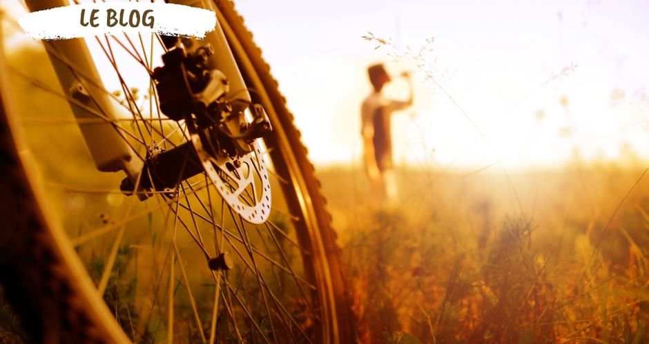 Cycliste buvant en arrière plan de son vélo, dans un champ baigné de soleil