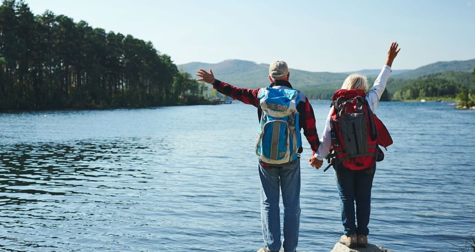 couple de randonneurs qui se tiennent la main de dos en observant devant eux un lac et ses sapins
