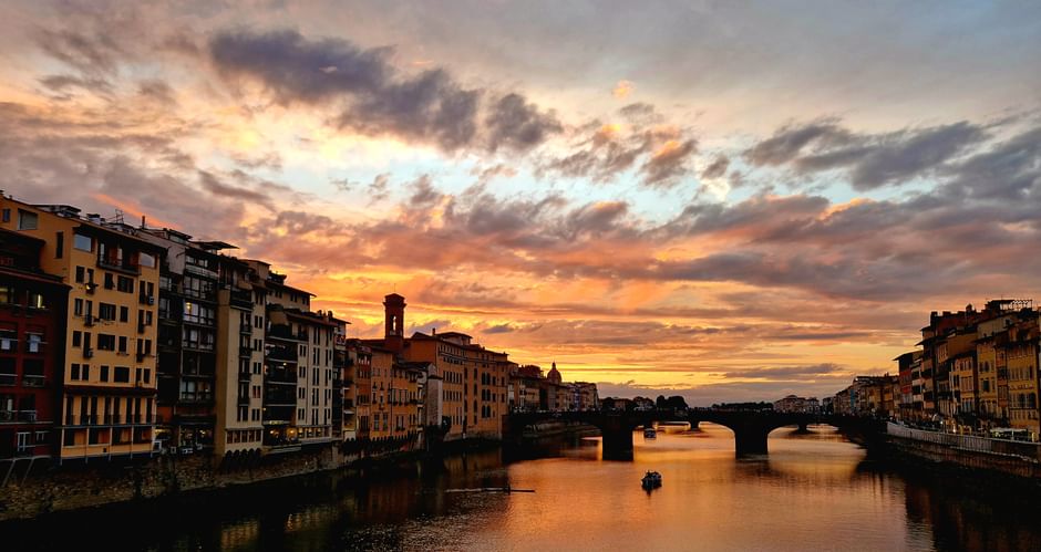 Coucher de soleil spectaculaire sur l'Arno à Florence avec des nuages colorés, des bâtiments historiques bordant les rives et un pont.