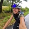 Cycliste souriante prenant un selfie sur une route de campagne mouillée en Toscane, portant un casque avec lunettes bleues et sac à dos.